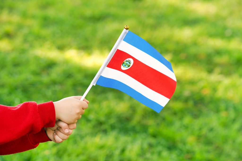 Hands of kid girl holding Costa Rica flag. Independence Day concept. Green grass background.